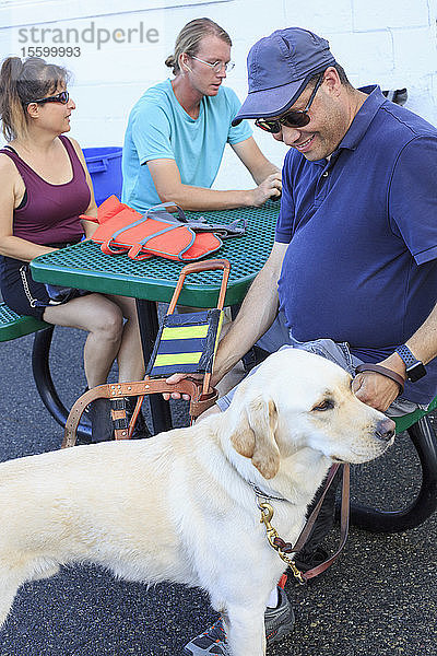 Ein blinder Mann und eine blinde Frau sitzen mit einem Diensthund und einem Segellehrer zusammen