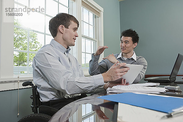 Geschäftsmann mit Rückenmarksverletzung im Gespräch mit seinem Kollegen in einem Büro