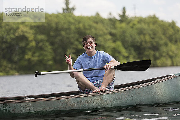 Glücklicher junger Mann mit Down-Syndrom rudert ein Kanu auf einem See