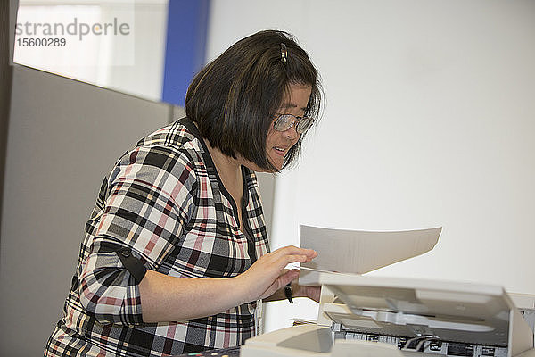 Asiatische Frau mit einer Lernbehinderung arbeitet an einem Kopiergerät im Büro