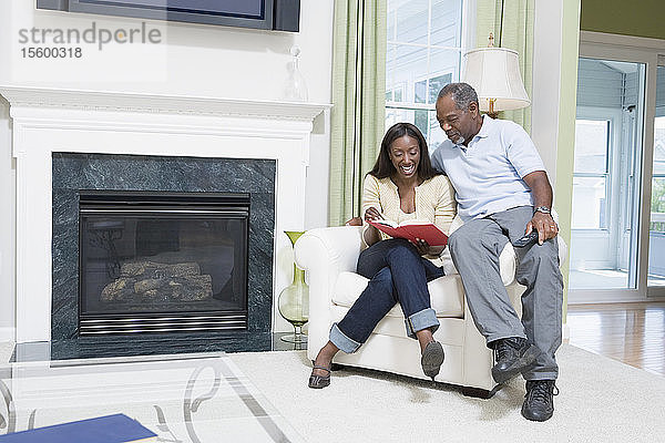 Ehepaar mittleren Alters sitzt in einem Sessel  schaut in ein Buch und lächelt