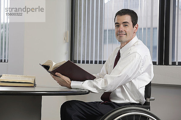 Geschäftsmann mit Rückenmarksverletzung hält ein Buch und lächelt