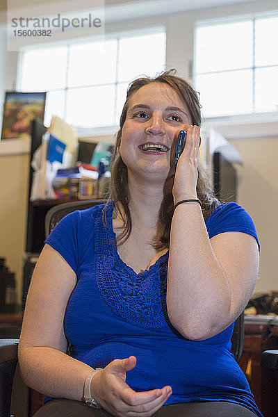 Junge Frau mit zerebraler Lähmung  die zu Hause mit ihrem Handy telefoniert