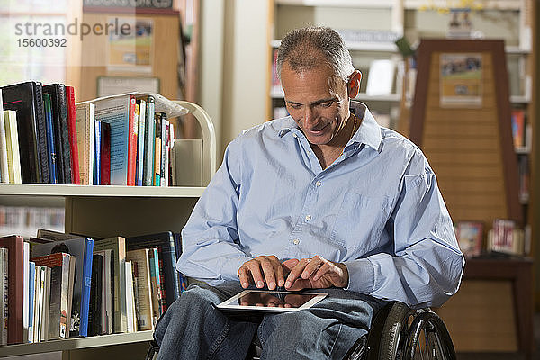 Mann mit Rückenmarksverletzung in einer Bibliothek mit Blick auf ein Tablet