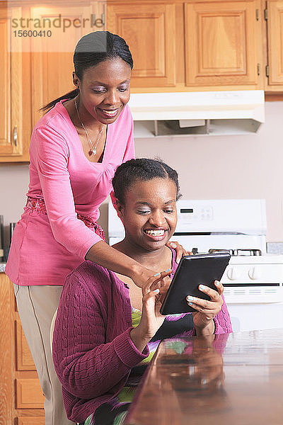 Zwei Schwestern  eine mit Lernbehinderung  schauen in der Küche auf ein digitales Tablet.