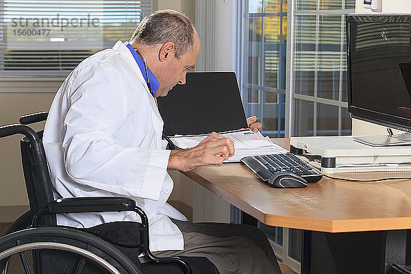 Mann mit Friedreich-Ataxie und deformierten Händen als Arzt  der an seinem Computer Patientenakten betrachtet