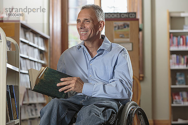 Mann im Rollstuhl mit einer Rückenmarksverletzung genießt ein Buch in einer Bibliothek