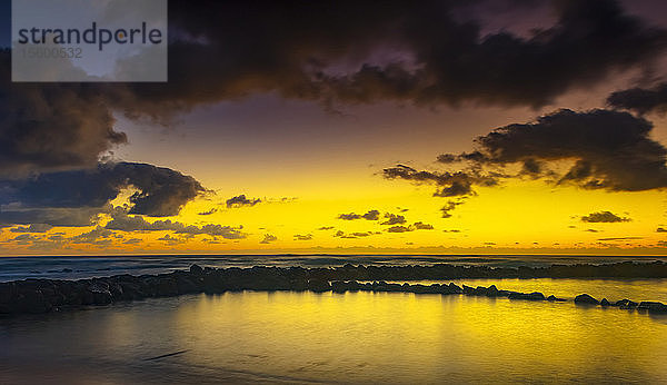 Goldener Sonnenaufgang über dem Lydgate Park und dem Ozean an der Küste von Kauai mit einem silhouettierten Wellenbrecher; Kapaa  Kauai  Hawaii  Vereinigte Staaten von Amerika