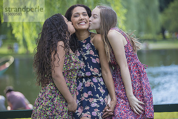 Glückliche hispanische Mutter wird von zwei Teenager-Töchtern im Park geküsst