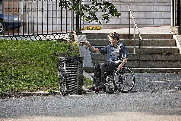 Ein Mann mit einer Rückenmarksverletzung im Rollstuhl wirft in einem öffentlichen Park Müll in einen Behälter
