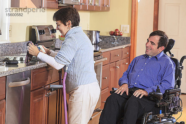 Frau mit Cerebralparese benutzt Krücken und arbeitet in ihrer Küche  während sie mit ihrem Mann mit Cerebralparese spricht