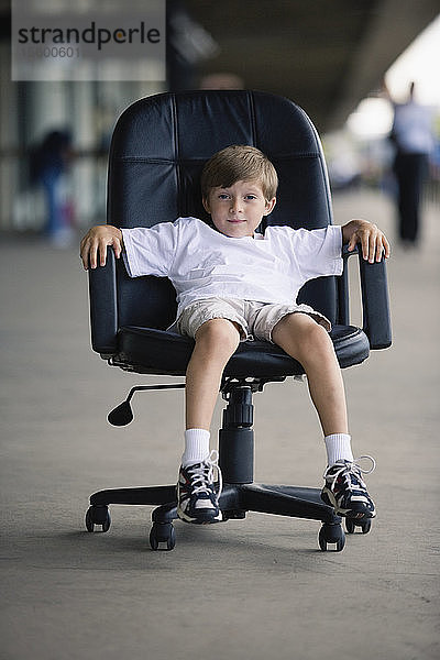 Porträt eines Jungen  der in einem Chefsessel sitzt.