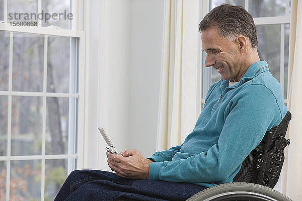 Mann sitzt im Rollstuhl und benutzt einen persönlichen Datenassistenten