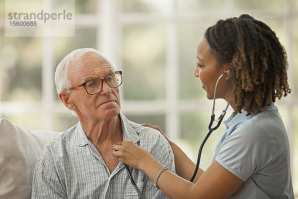 Nachdenklicher älterer Mann  dessen Herzschlag von einer Krankenschwester abgehört wird.