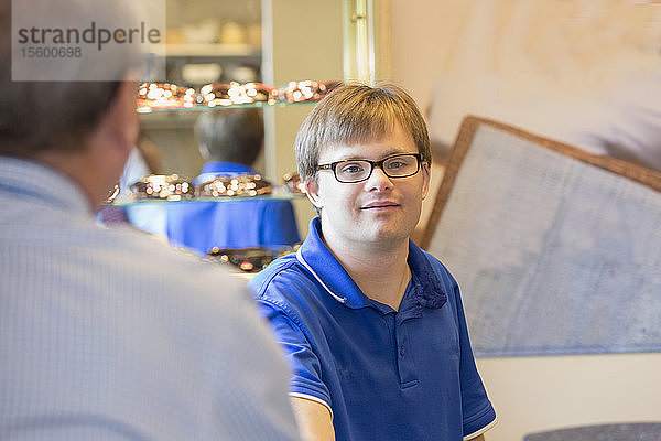 Junger Mann mit Down-Syndrom bei der Arbeit in der Abteilung für Brillenanpassung in einer Gesundheitsklinik