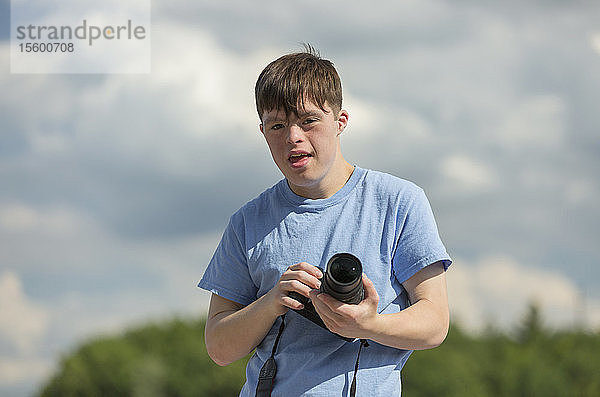 Junger Mann mit Down-Syndrom hält eine Kamera