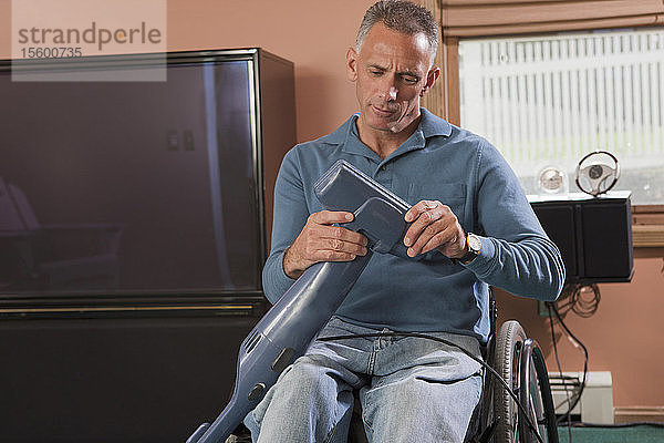 Mann mit Querschnittslähmung im Rollstuhl beim Staubsaugen