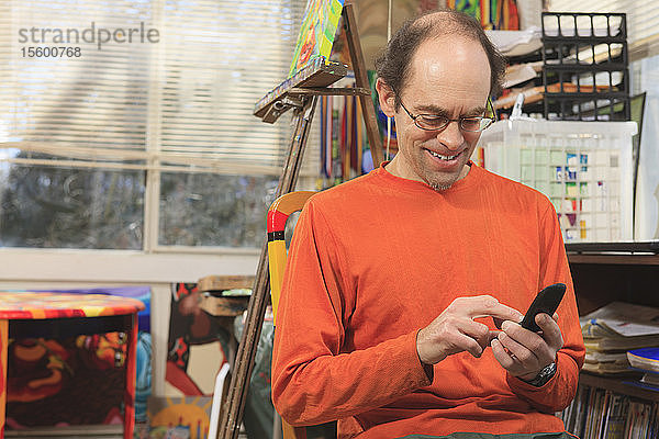 Mann mit Asperger-Syndrom in seinem Malatelier mit seinem Mobiltelefon