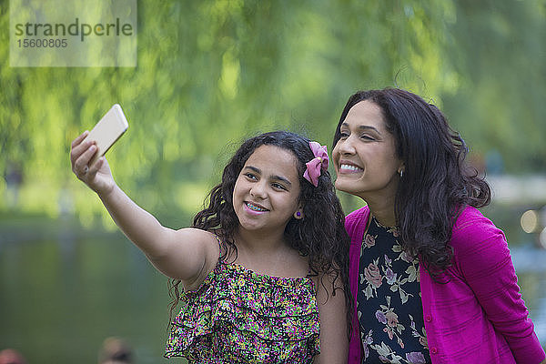 Glückliche hispanische Mutter mit Teenager-Tochter mit Zahnspange  die ein Selfie mit Handy im Park macht