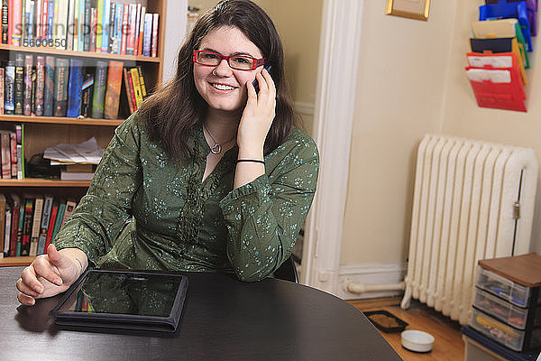 Frau mit Asperger-Syndrom arbeitet mit ihrem Smartphone und Tablet im Heimbüro