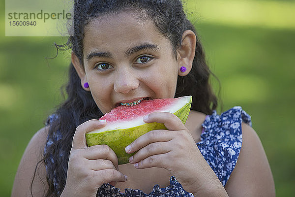 Porträt eines glücklichen hispanischen Teenagers mit Zahnspange  der eine Wassermelone isst
