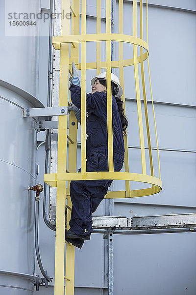 Eine Ingenieurin klettert in einem Kraftwerk in einem Sicherheitskäfig auf eine Leiter