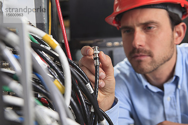 Netzwerktechniker  der eine BNC-Kabelverbindung an einer Schalttafel hält