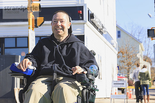 Mann mit Rückenmarksverletzung und Arm mit Nervenschaden im motorisierten Rollstuhl überquert beim Einkaufen eine öffentliche Straße