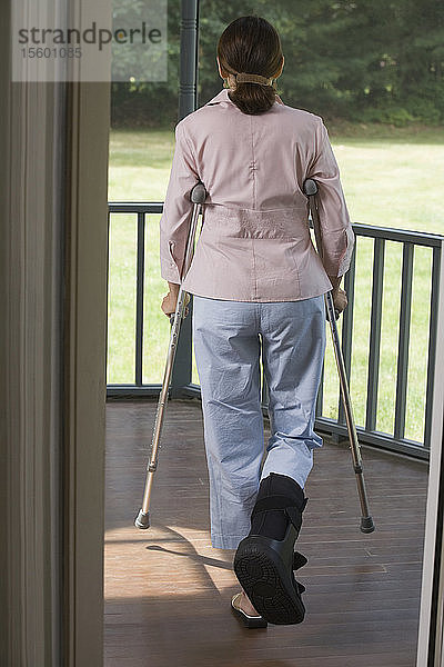 Rückansicht einer Frau  die mit Krücken auf einem Balkon geht