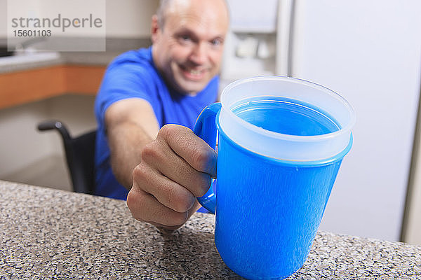 Mann mit Friedreich-Ataxie  der mit seinen deformierten Händen eine Tasse Wasser hält