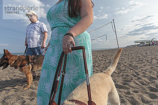 Junges Paar mit Sehbehinderung und Diensthunden beim Spaziergang am Strand