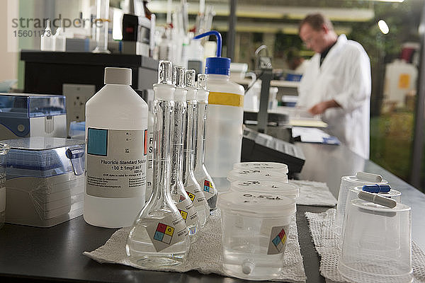 Kolben mit Proben- und Reagenzienflaschen in einem Labor mit einem Wissenschaftler im Hintergrund
