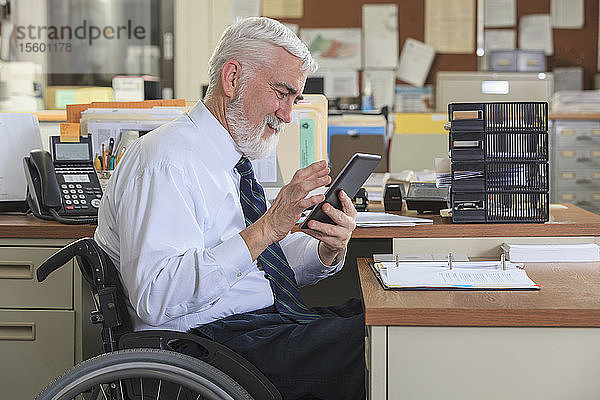 Mann mit Muskeldystrophie im Rollstuhl benutzt ein Tablet an seinem Bürotisch