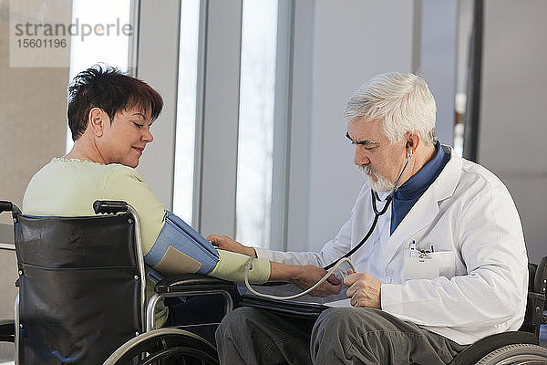 Arzt mit Muskeldystrophie im Rollstuhl prüft den Blutdruck eines Patienten