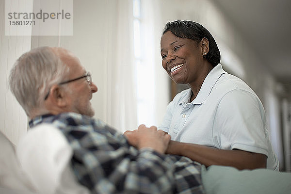 Glückliche Krankenschwester tröstet einen älteren Patienten am Krankenbett