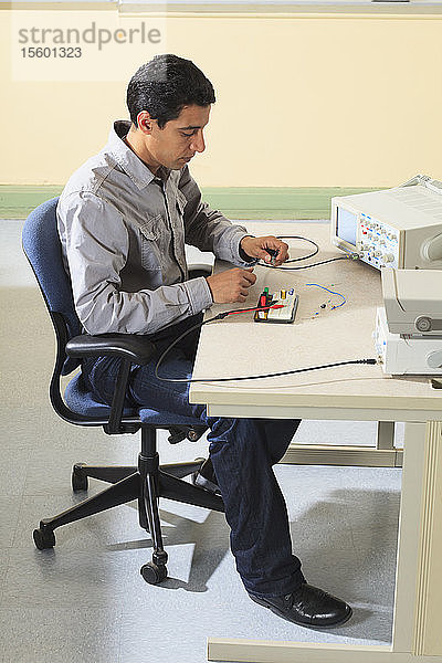 Ein Student der Ingenieurwissenschaften schließt ein Oszilloskop an ein Prototyping-Breadboard an  um ein Experiment für ein Elektroniklabor zu messen