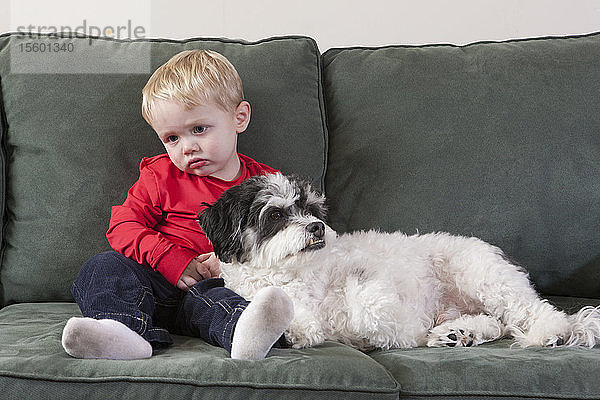 Müder Junge sitzt mit einem Hund auf einer Couch
