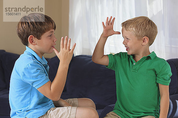 Jungen mit einer Hörbehinderung  die auf ihrer Couch in amerikanischer Gebärdensprache Mama  Papa oder Eltern gebärden