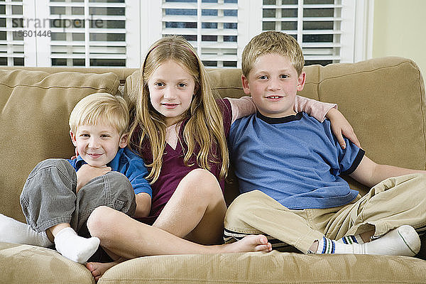 Porträt von drei Kindern  die auf einem Sofa sitzen.
