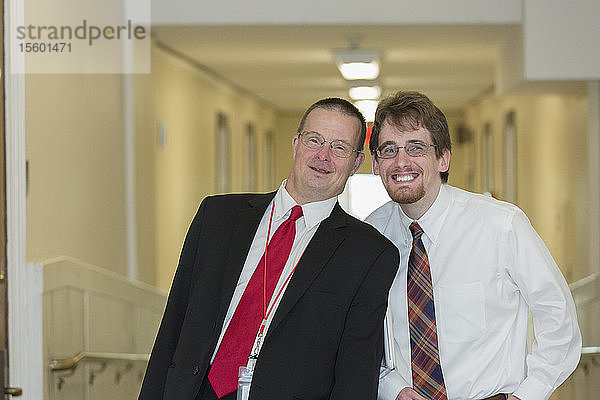 Porträt eines Mannes mit Down-Syndrom  der mit einem Mitarbeiter im Bürokorridor des State Capitol lächelt