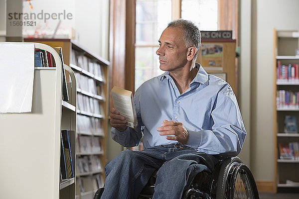 Mann im Rollstuhl mit einer Rückenmarksverletzung ordnet Bücher in einer Bibliothek