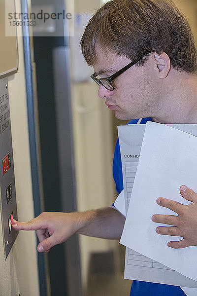 Junger Mann mit Down-Syndrom benutzt den Aufzug  während er in einer Klinik Papierkram abliefert