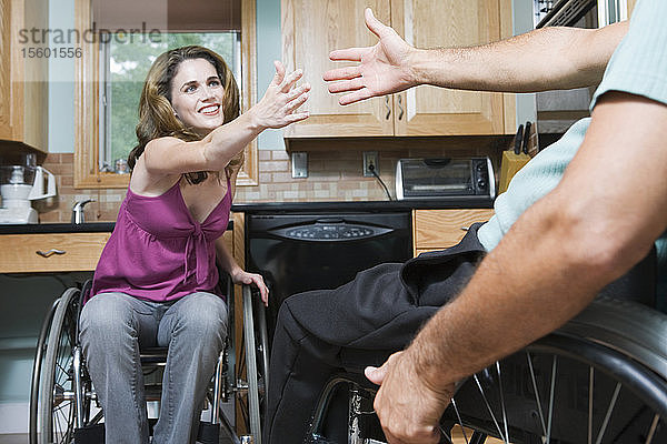 Mittlere erwachsene Frau  die in einem Rollstuhl sitzt und nach der Hand einer anderen Person greift