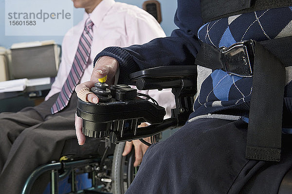 Geschäftsmann mit Duchenne-Muskeldystrophie benutzt einen motorisierten Rollstuhl neben seinem Kollegen mit Rückenmarksverletzung