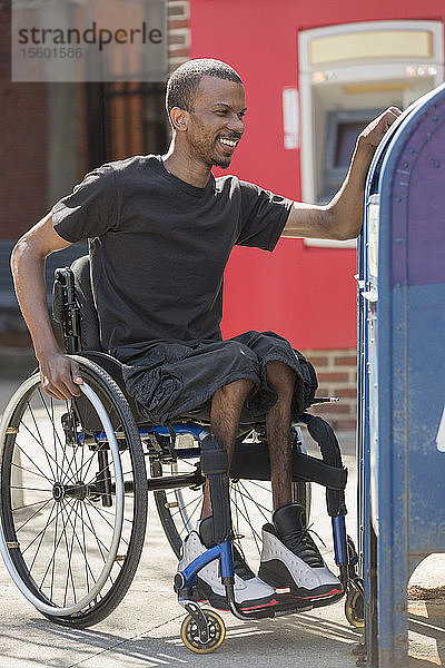 Mann im Rollstuhl  der an Spinaler Meningitis erkrankt ist  benutzt den öffentlichen Briefkasten