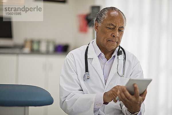 Nachdenklicher männlicher Arzt  der ein digitales Tablet benutzt  während er in seinem Büro sitzt.