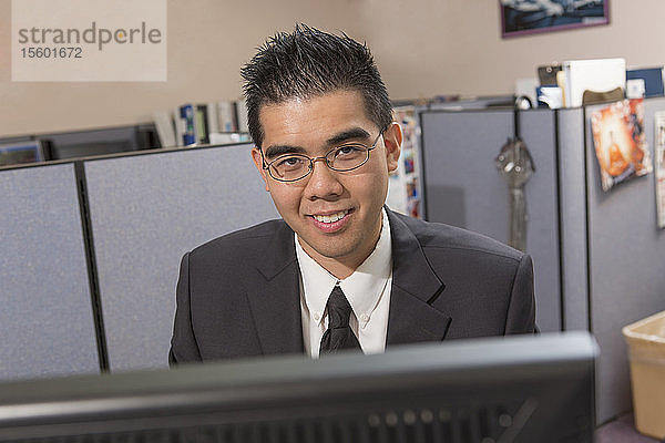 Porträt eines glücklichen asiatischen Mannes mit Autismus  der in einem Büro am Computer arbeitet