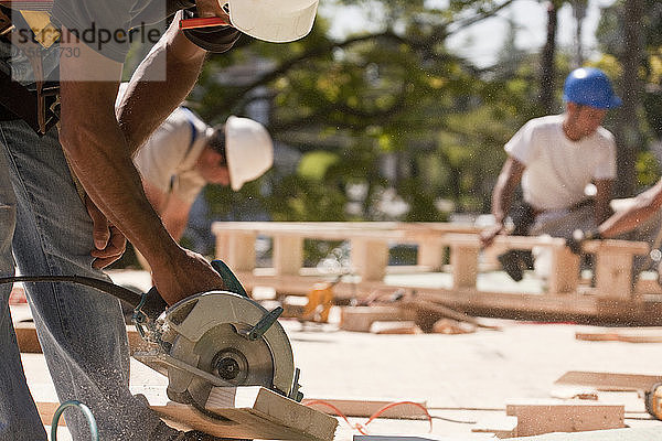 Zimmerleute bei der Arbeit mit einer Kreissäge auf einer Baustelle mit Giebelrahmen im Hintergrund