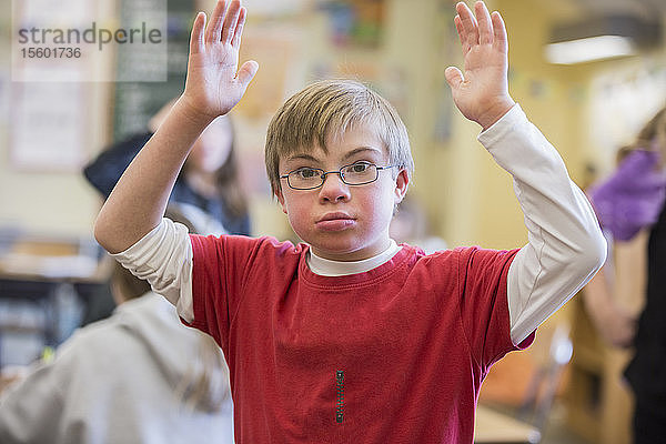 Junge mit Down-Syndrom mit erhobenen Armen in einem Klassenzimmer