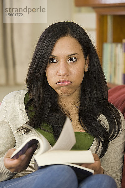 Hispanische Frau sitzt auf einer Couch und hält ein Buch